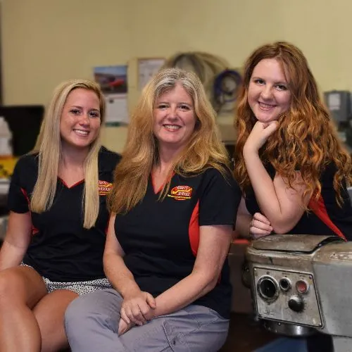 Three members of the company team in company shirts, seated beside a piece of equipment in the shop