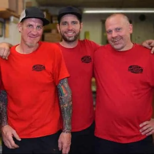 Three technicians in company shirts standing together in the company's shop